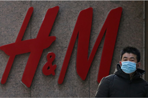Wearing a face mask walks by a Swedish fashion brand H&M store outlet Wearing a face mask walks by a Swedish fashion brand H&M store outlet